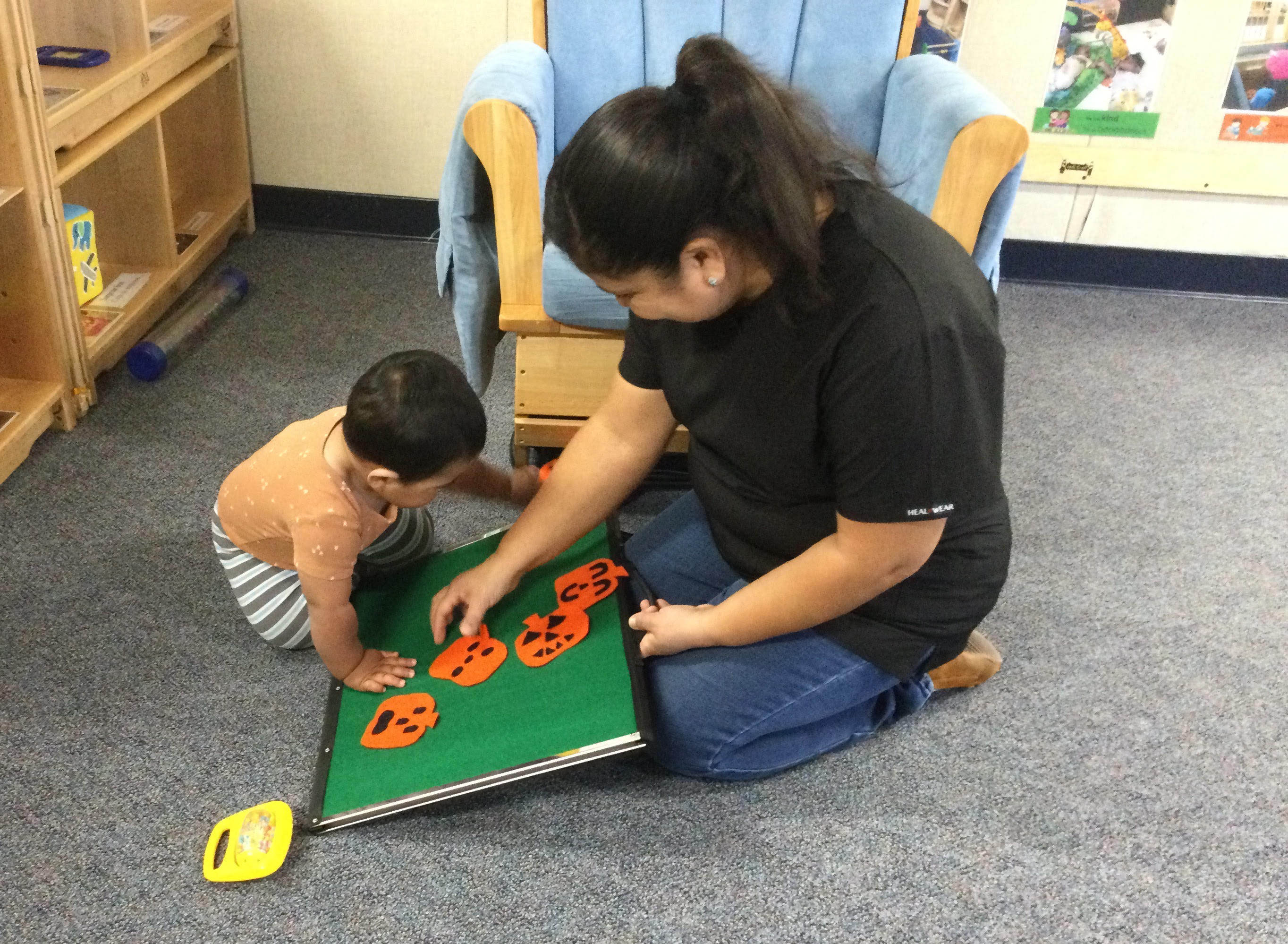 Teacher sitting on the floor with an infant playing with pumpkins on a felt board